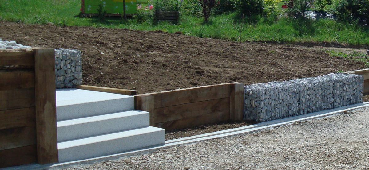 Muret dans le jardin en madriers de bois, et retenue de terre avec des gabions. A côté, il y a l'escalier en pierre de Granit gris. C'est un aménagement de jardin réalisé à Boege en Vallée Verte.